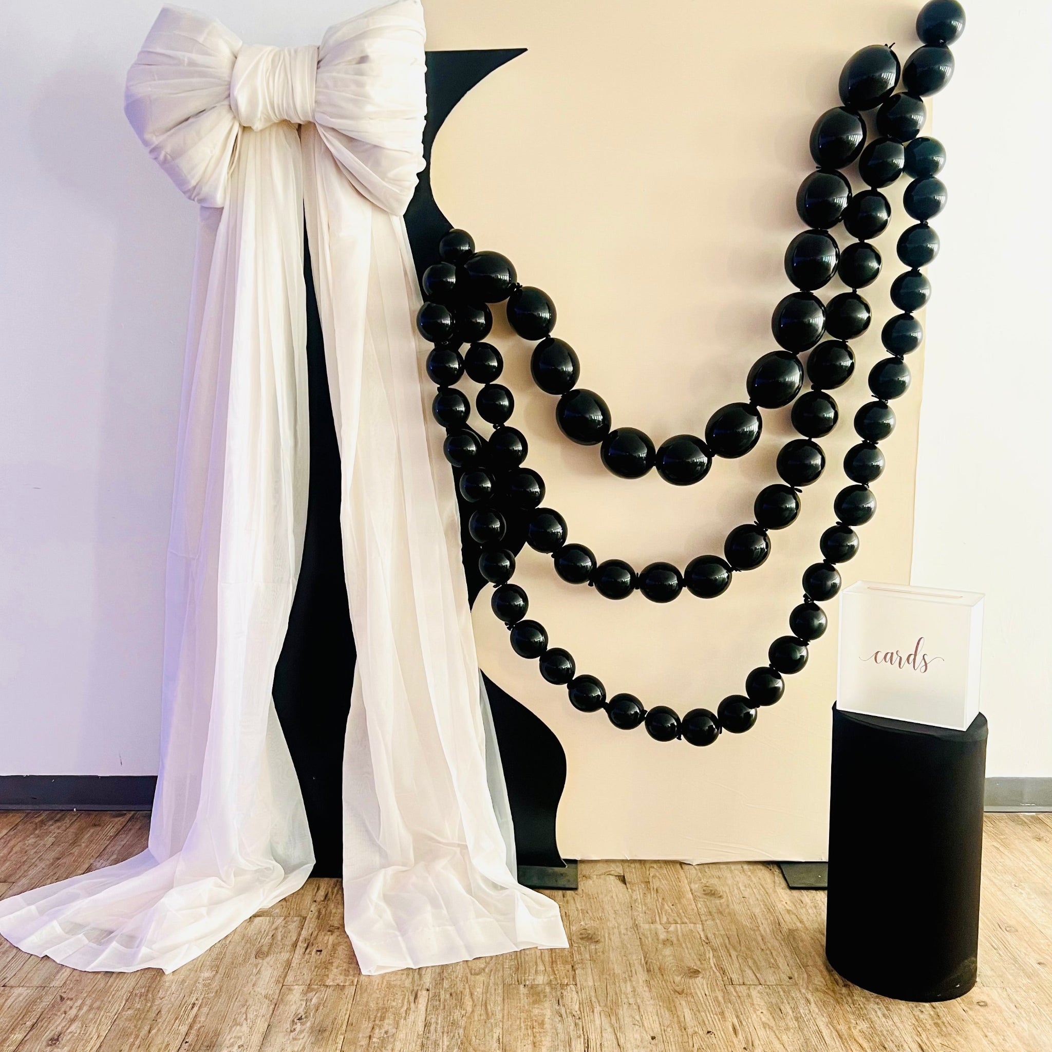 Black Linking beaded balloons hanging  on a elegant party birthday cream color backdrop with a white bow.